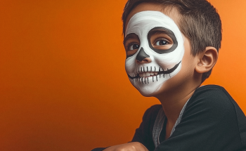 Enfant souriant avec un maquillage de squelette blanc et noir sur le visage, sur fond orange, ambiance Halloween festive