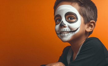 Enfant souriant avec un maquillage de squelette blanc et noir sur le visage, sur fond orange, ambiance Halloween festive